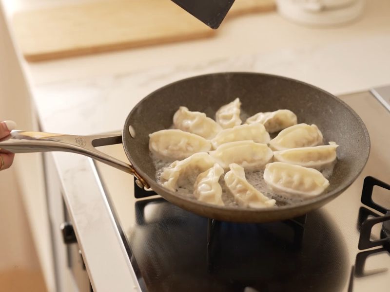 devojka prži nešto u tiganju na šporetu